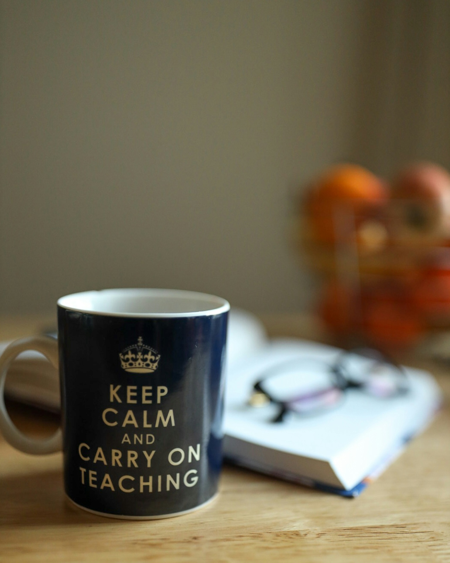 Navy mug reading 'Keep Calm and Carry On Teaching' beside an open notebook and glasses